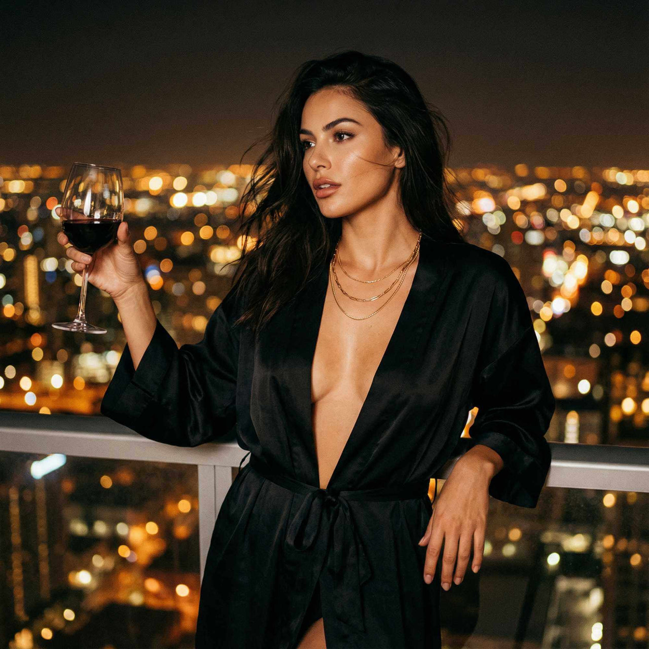 Model wearing the Saona Triple Layer Necklace by Brother & Sisters, holding a glass of wine, city lights in background.