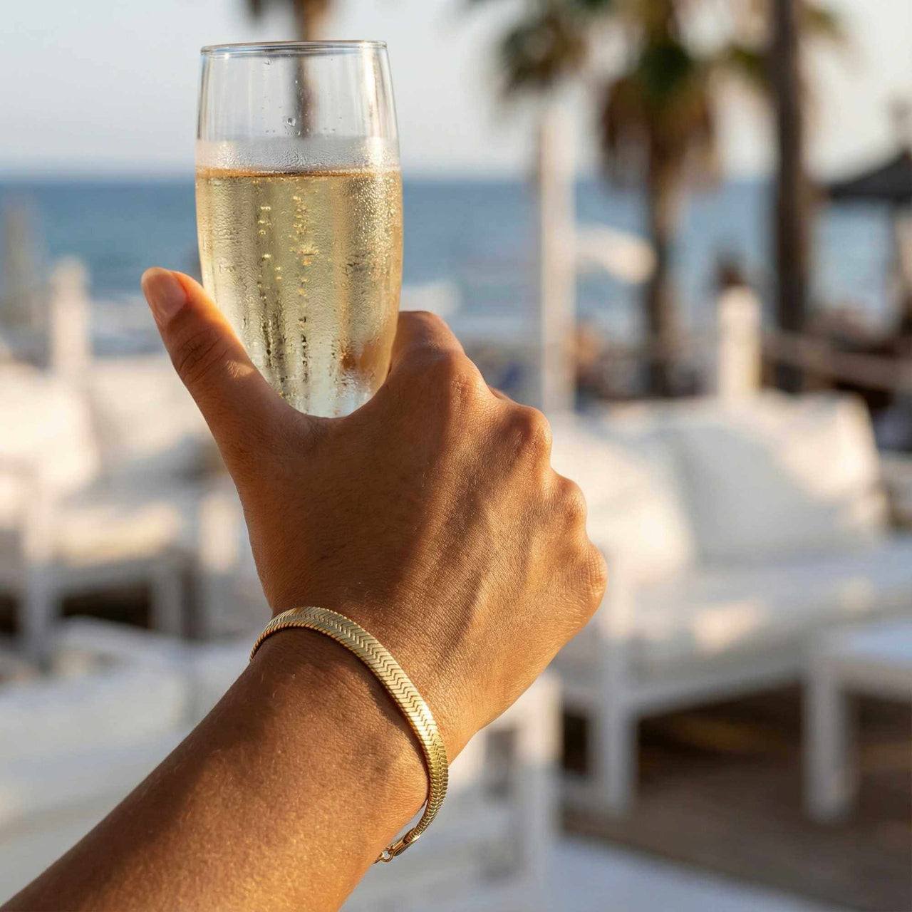 Person holding a champagne glass, wearing the Kauai Herringbone Bracelet by Brother & Sisters, showcasing elegance and style.