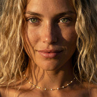 Thumbnail for Close-up of a woman wearing a White Beaded Choker by Brother & Sisters, featuring white enamel beads and a delicate gold chain.