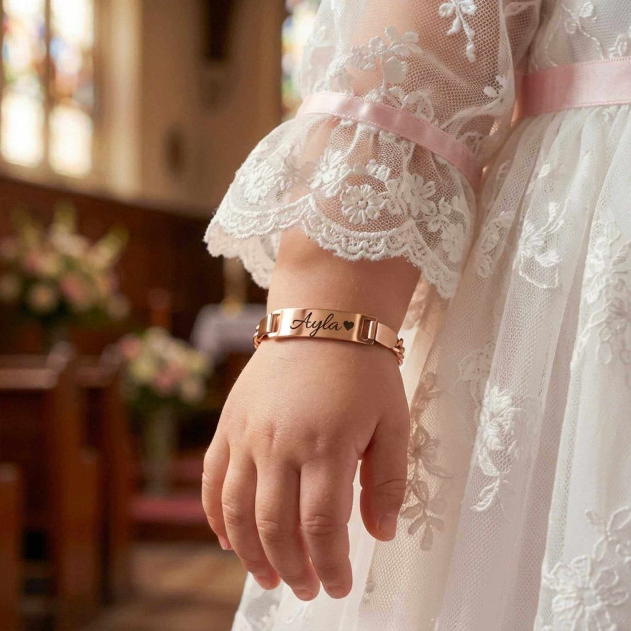 Infant Bracelet by Brother & Sisters featuring a personalized name, worn by a baby in a beautiful dress.
