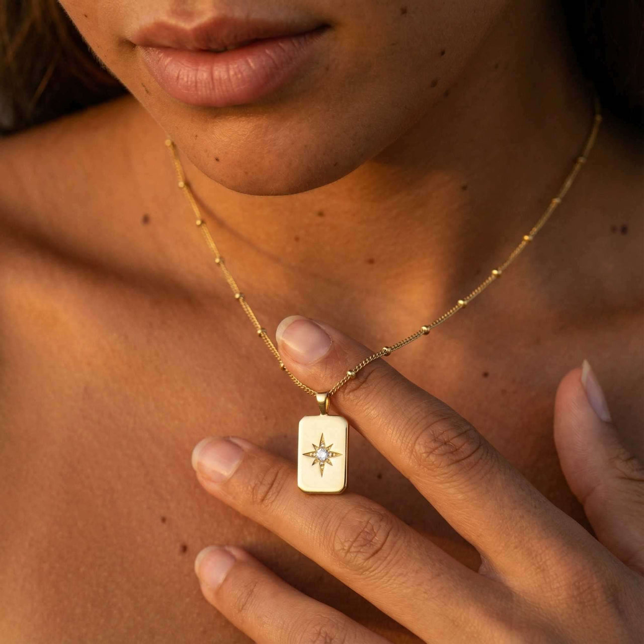 Starlight Pendant Necklace worn by a woman, featuring a gold tag pendant with a starburst and zirconia stone, Brother & Sisters.