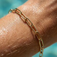Thumbnail for Close-up of a hand wearing a Paperclip Chain Bracelet by Brother & Sisters, showcasing its sleek gold links.