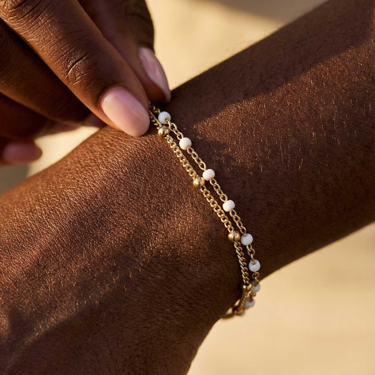 Close-up of a model wearing the Double White Bracelet by Brother & Sisters, featuring gold links and white enamel beads.