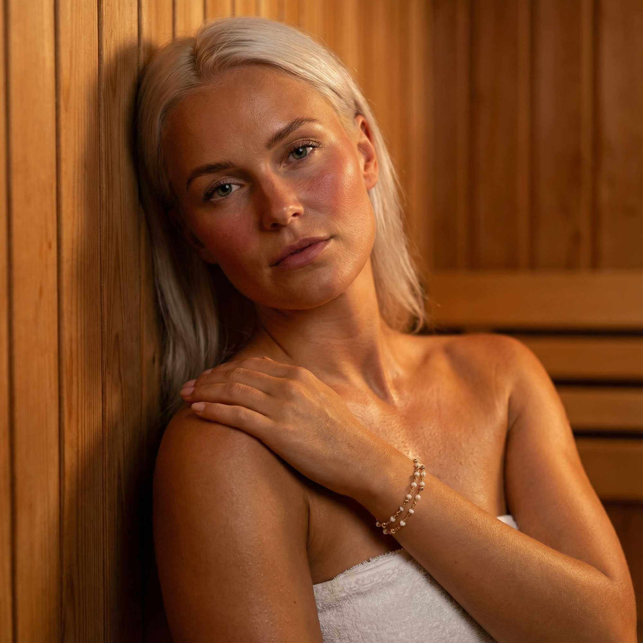 Double White Bracelet worn by a model with pale skin in a wooden sauna, showcasing its elegant design from Brother & Sisters.