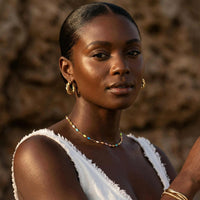 Thumbnail for A model wearing the Rainbow Choker by Brother & Sisters, featuring colorful enamel beads and a gold chain.