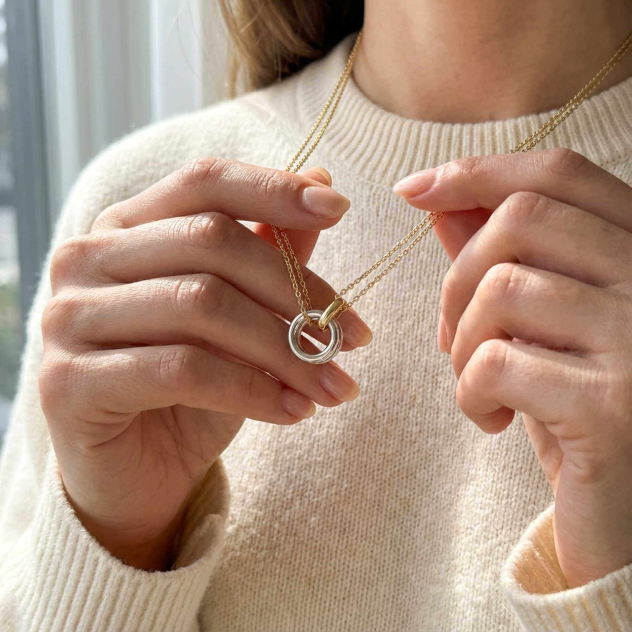 A woman showcases The Unity Bond necklace by Brother & Sisters, featuring a silver circle and gold bar pendant.