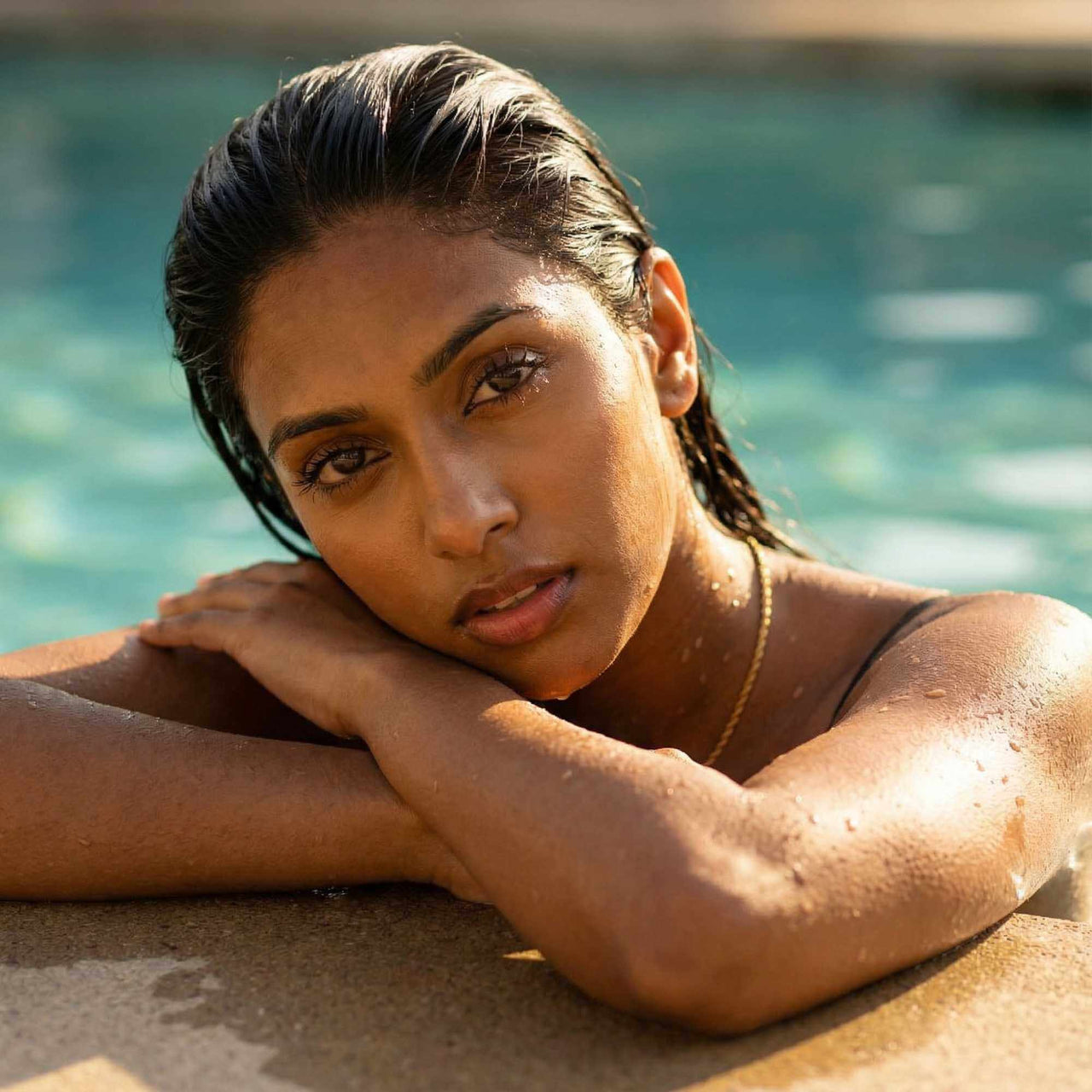 Woman relaxing by the pool wearing a delicate necklace, showcasing effortless beauty and natural glow.