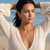 Thumbnail for Starlight Pendant Necklace worn by model at the beach, featuring a polished gold pendant with starburst and zirconia stone by Brother & Sisters.