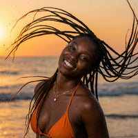Thumbnail for Happy woman with braided hair wearing La Isla Pearl Toggle Necklace, smiling at sunset by the sea.