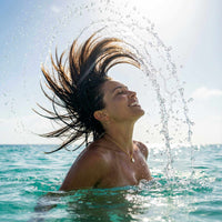 Thumbnail for Woman enjoying the ocean with hair splashing water, wearing the Astra Teardrop Necklace by Brother & Sisters.