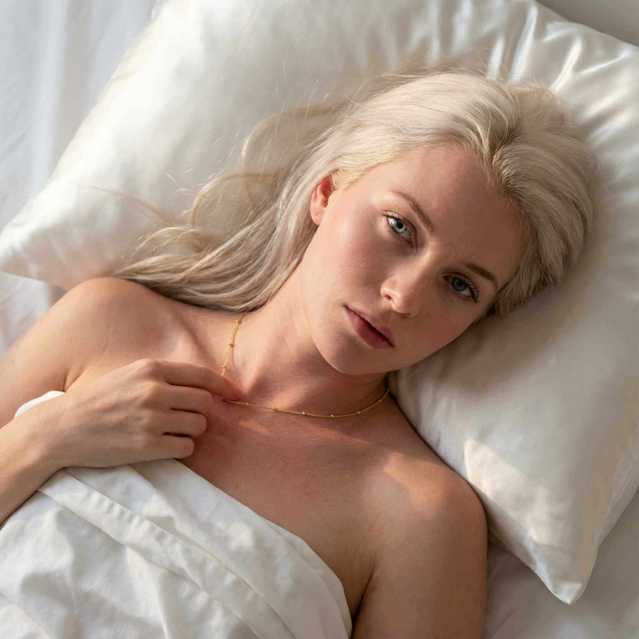 Julia Beaded Chain Necklace worn by a model resting on a pillow, showcasing its delicate golden beads.