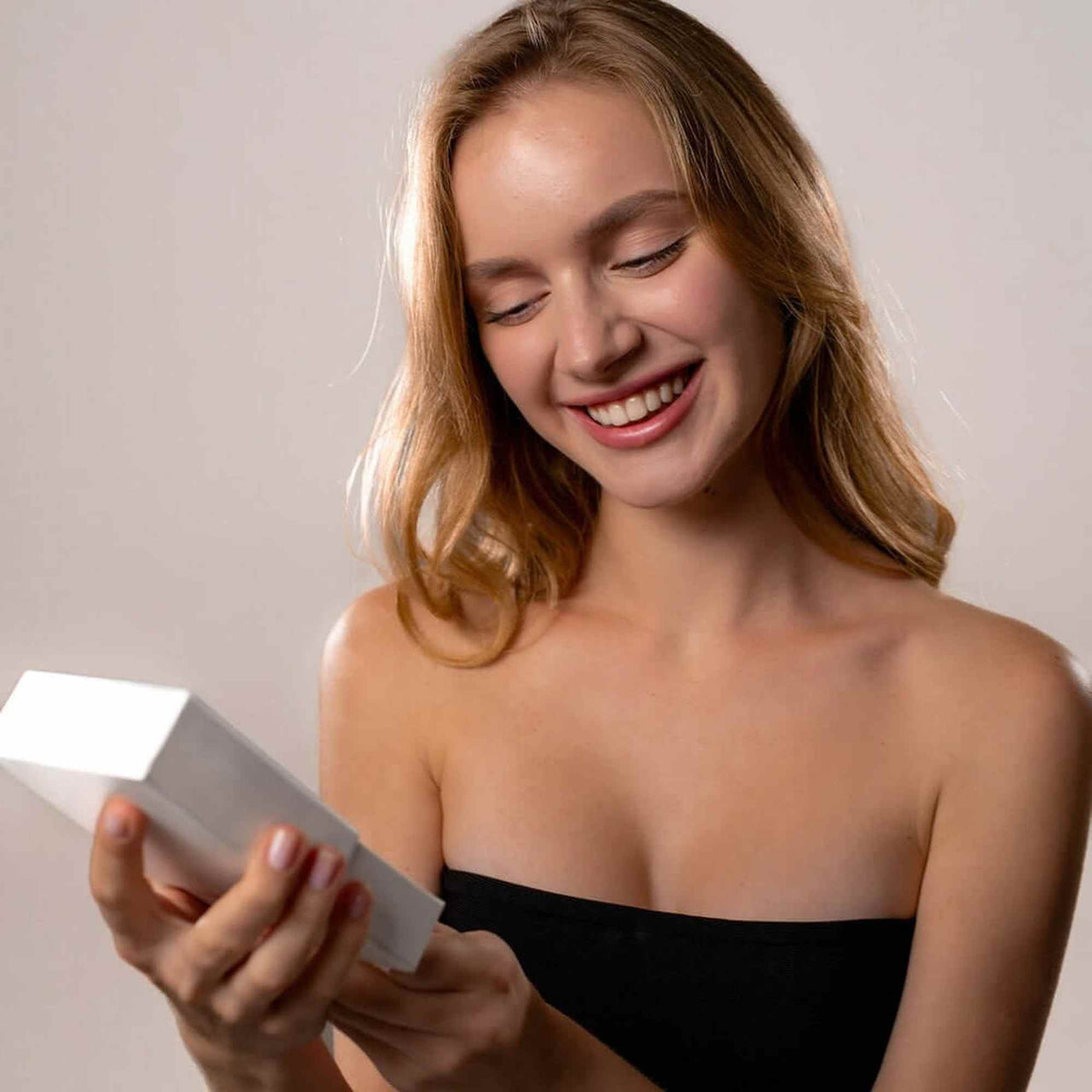 Smiling woman holding a gift box, excited to unveil the Love Photo Necklace by Brother & Sisters.