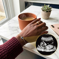 Thumbnail for Photo Projection Bracelet showcasing ultrasound image, worn by a mother enjoying coffee, by Brother & Sisters.
