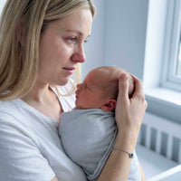 Thumbnail for A mother holding her newborn baby, wearing a Photo Projection Bracelet by Brother & Sisters, capturing precious memories.