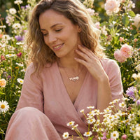 Thumbnail for Daisy Name Necklace worn by a woman in a flower field, featuring three hearts and a delicate enamel daisy by Brother & Sisters.
