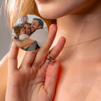 Thumbnail for Woman holding an Angel Photo Necklace with a family photo, designed by Brother & Sisters, showcasing elegant angel wings.