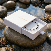 Thumbnail for Gold & Onyx Bead Anklet in a luxurious Brother & Sisters box by the water, showcasing its elegance and sophistication.