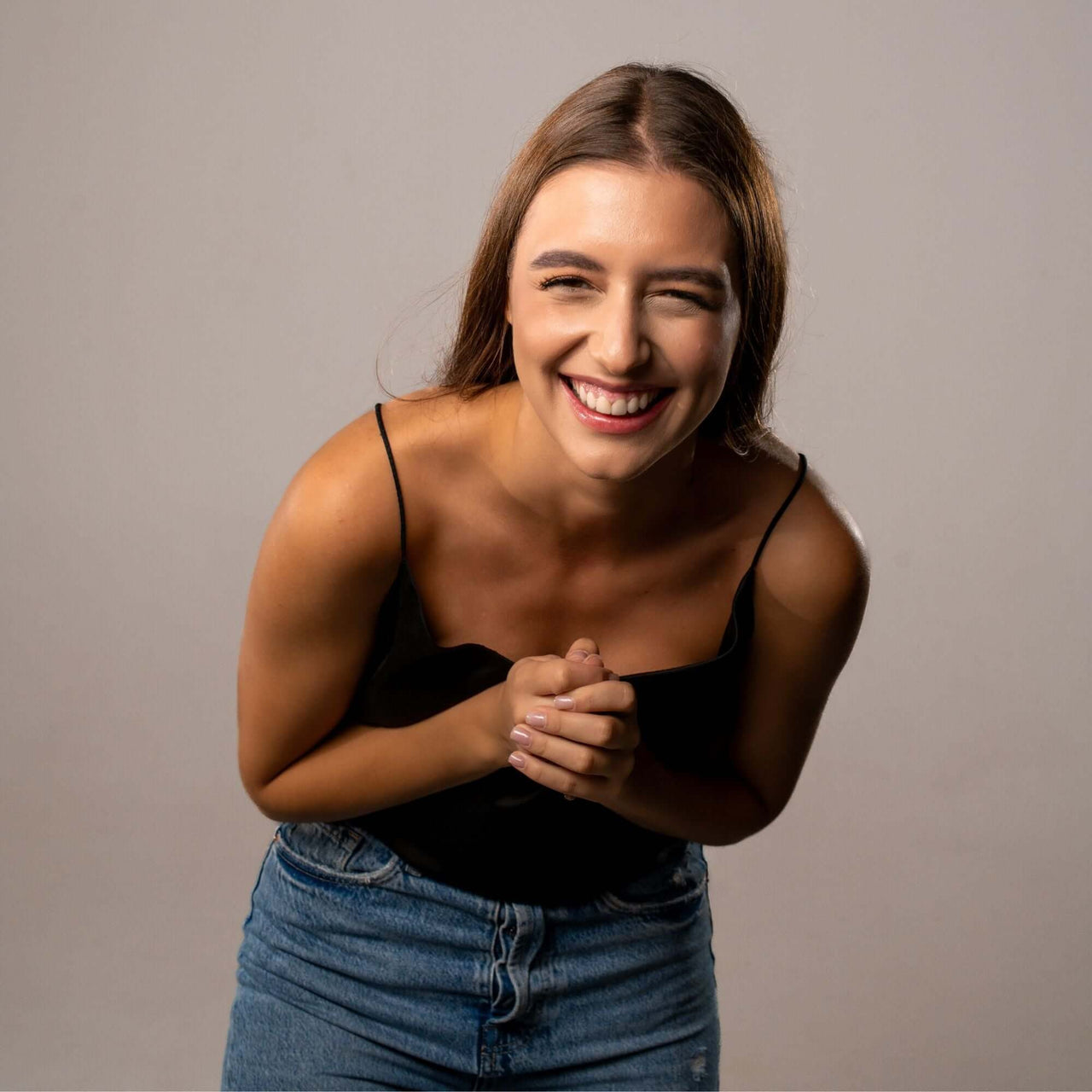 Smiling woman wearing a black top and jeans, showcasing joy and positivity in a cheerful portrait.