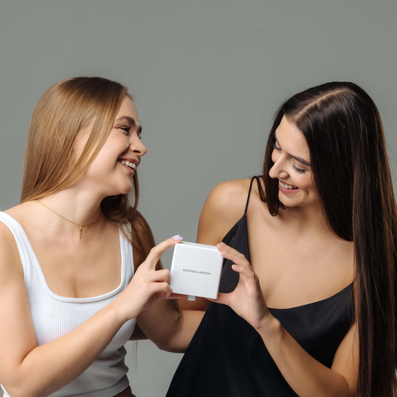 Two friends joyfully unboxing the Heart Name Necklace by Brother & Sisters, showcasing personal style and thoughtful gifting.