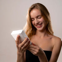 Thumbnail for A woman happily holding a gift box, representing the joy of receiving the Angel Photo Bracelet from Brother & Sisters.