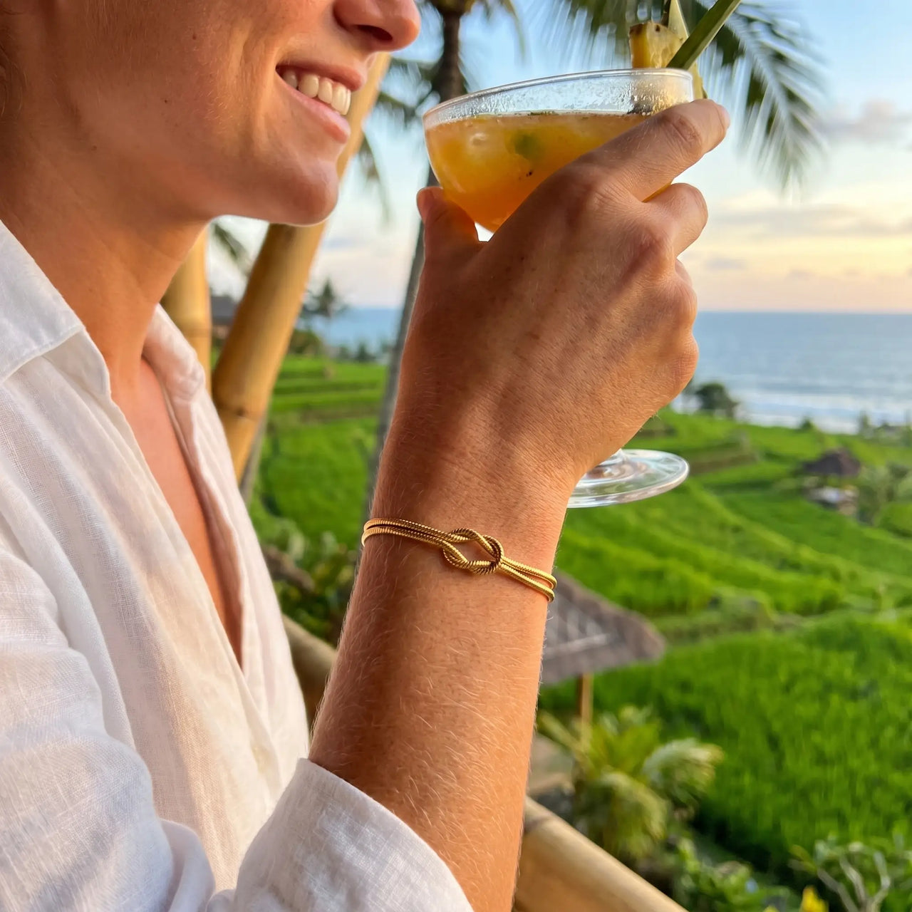Knot Couple Bracelet gold worn with cocktail at Bali rice terrace restaurant golden hour