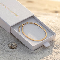 Thumbnail for Layla gold anklet inside B&S signature white slide-drawer gift box on beach sand at golden hour with sea shell — flat herringbone snake chain visible as continuous oval, luxury anklet packaging