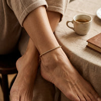 Thumbnail for Maëlle delicate gold tube-mesh anklet on mature Italian woman crossed ankle in villa interior with espresso and book — mature serene elegance