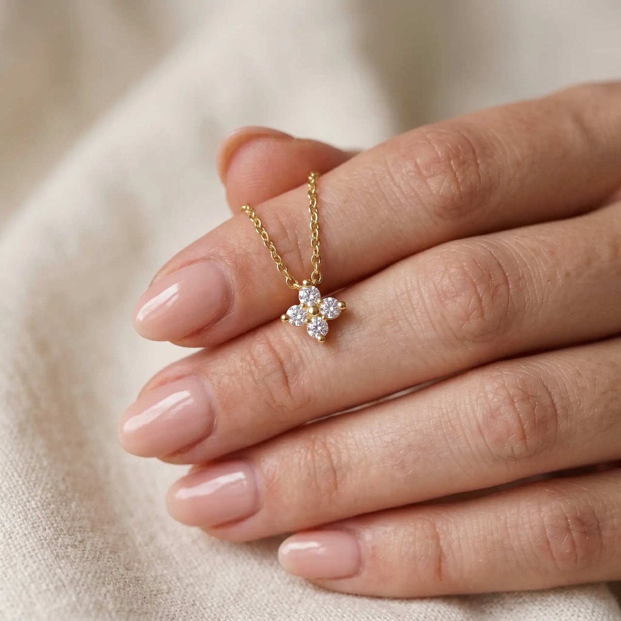 Crystal Flower necklace held between feminine fingertips with natural nude manicure — refined dainty perfection scale reveal