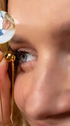 Close-up image of a person's hand holding a small golden charm pendant attached to a fine chain near their eye. A circular inset photo shows a mother and her young son smiling happily together, symbolizing a deeply personal and cherished memory.
