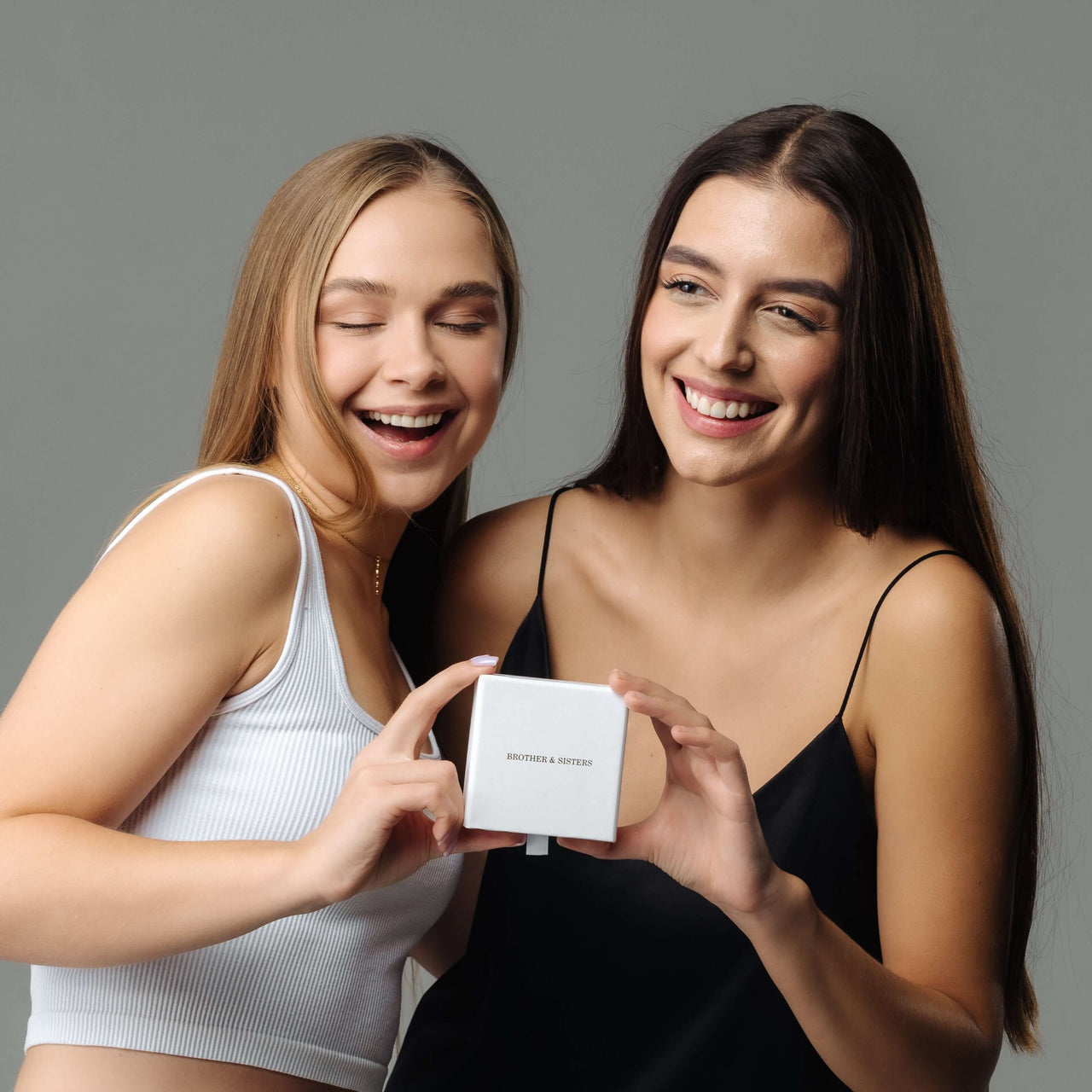 Two women joyfully holding a gift box from Brother & Sisters, highlighting the Lovers Name Necklace.