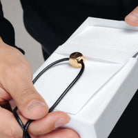 Thumbnail for Cube Initial Necklace held in hand, featuring a gold cube pendant and black cord, by Brother & Sisters.