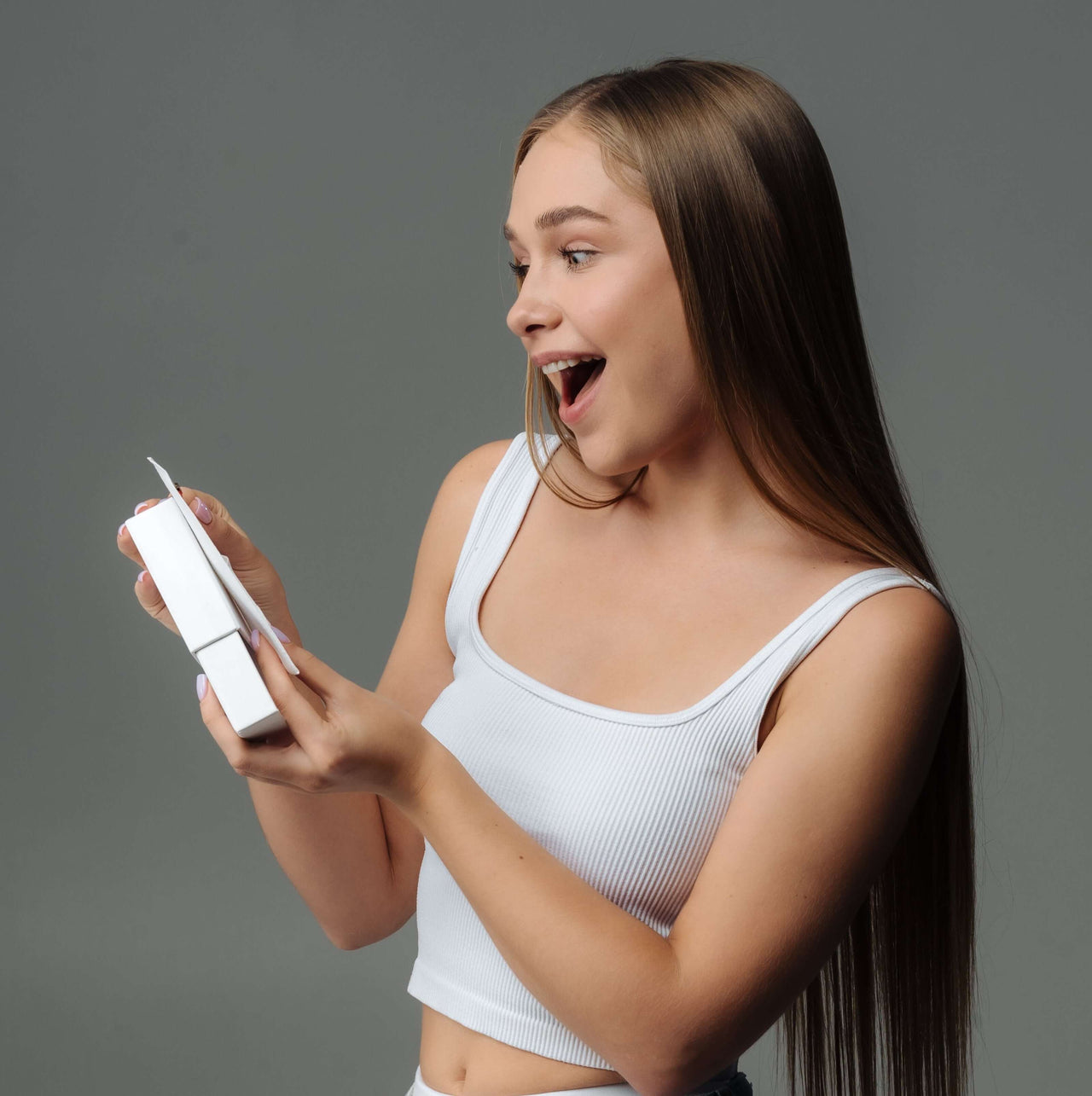 Young woman joyfully unwrapping a gift, showcasing excitement and surprise.