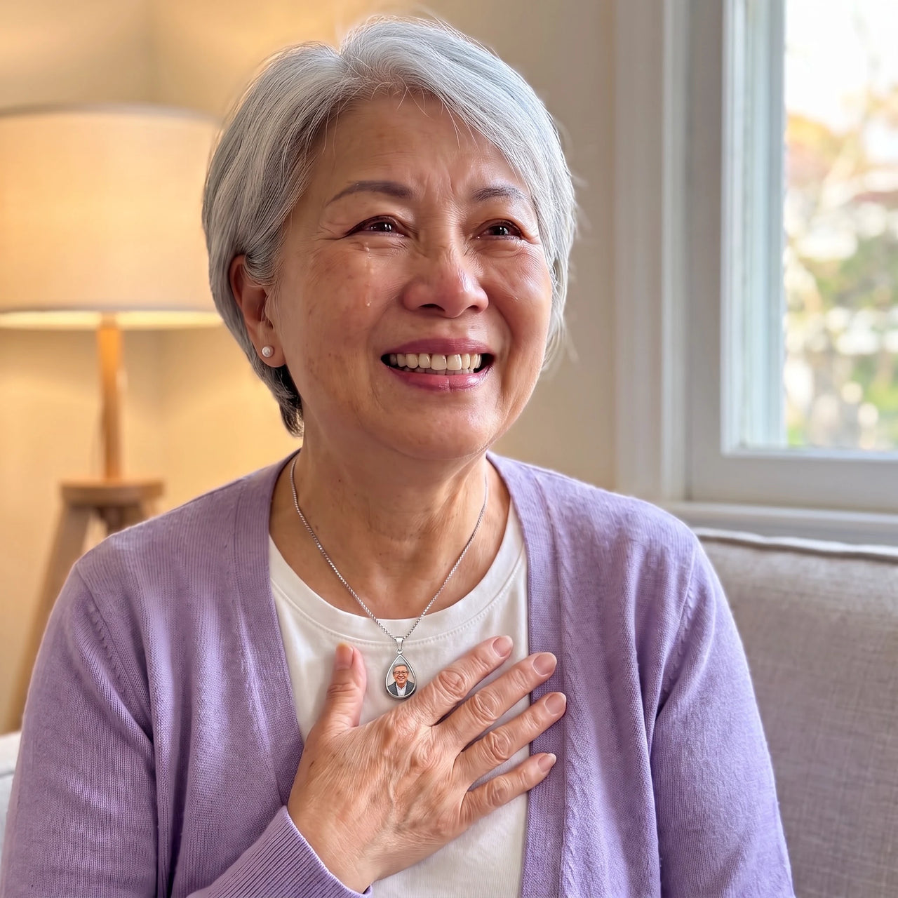 Smiling grey-haired woman in a lilac cardigan, hand on her heart, wearing the silver secret drop photo necklace | SKU: TPH-DRPN-SILVER