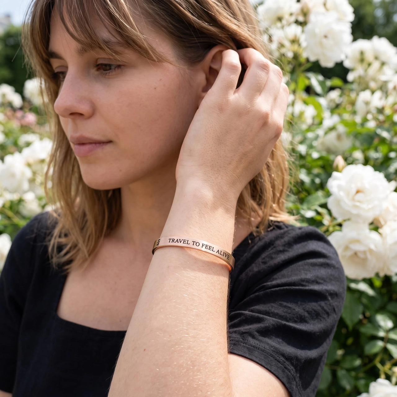 Woman gently touching her Travel To Feel Alive bracelet in rose gold | SKU: ttfa-rg